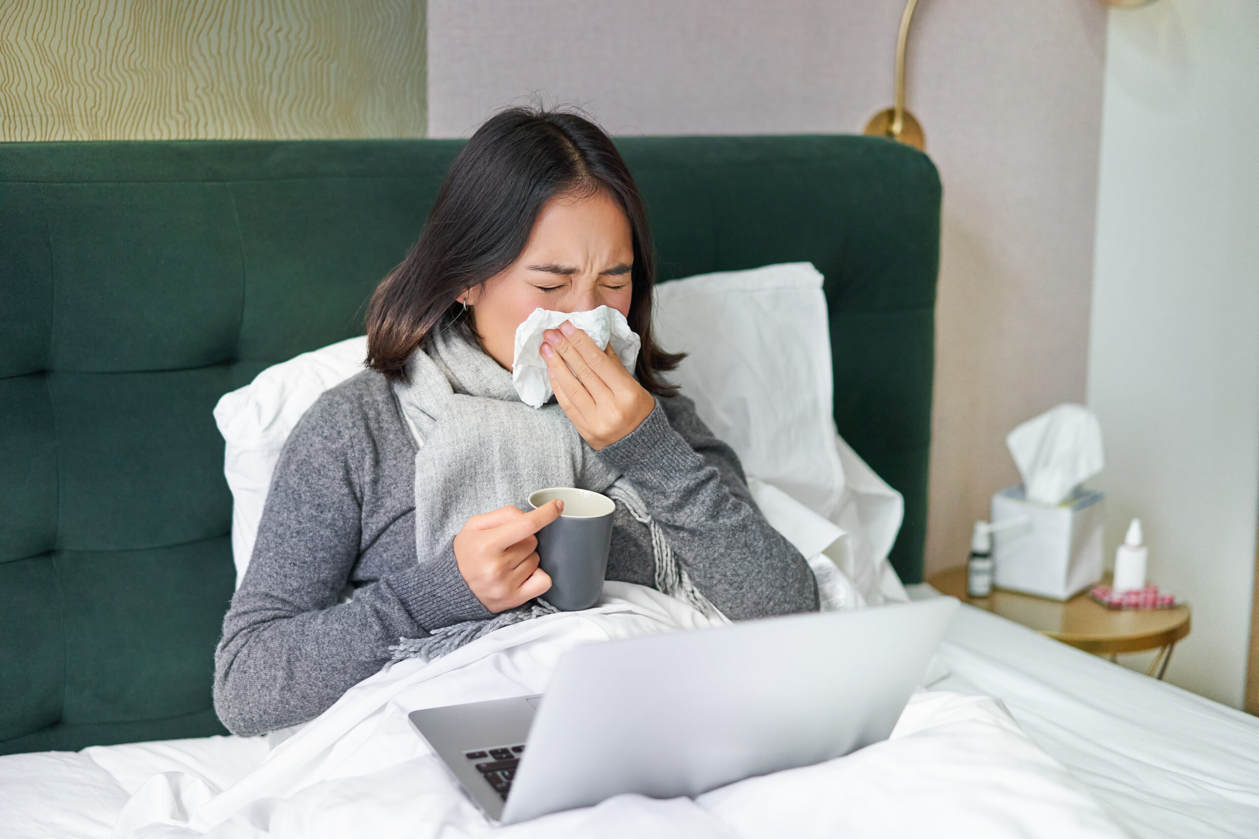 Woman with cold, having flu, staying in bed, sneezing in napkin, runny nose and influenza symptoms