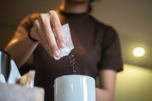 Person pouring sweetener into a mug