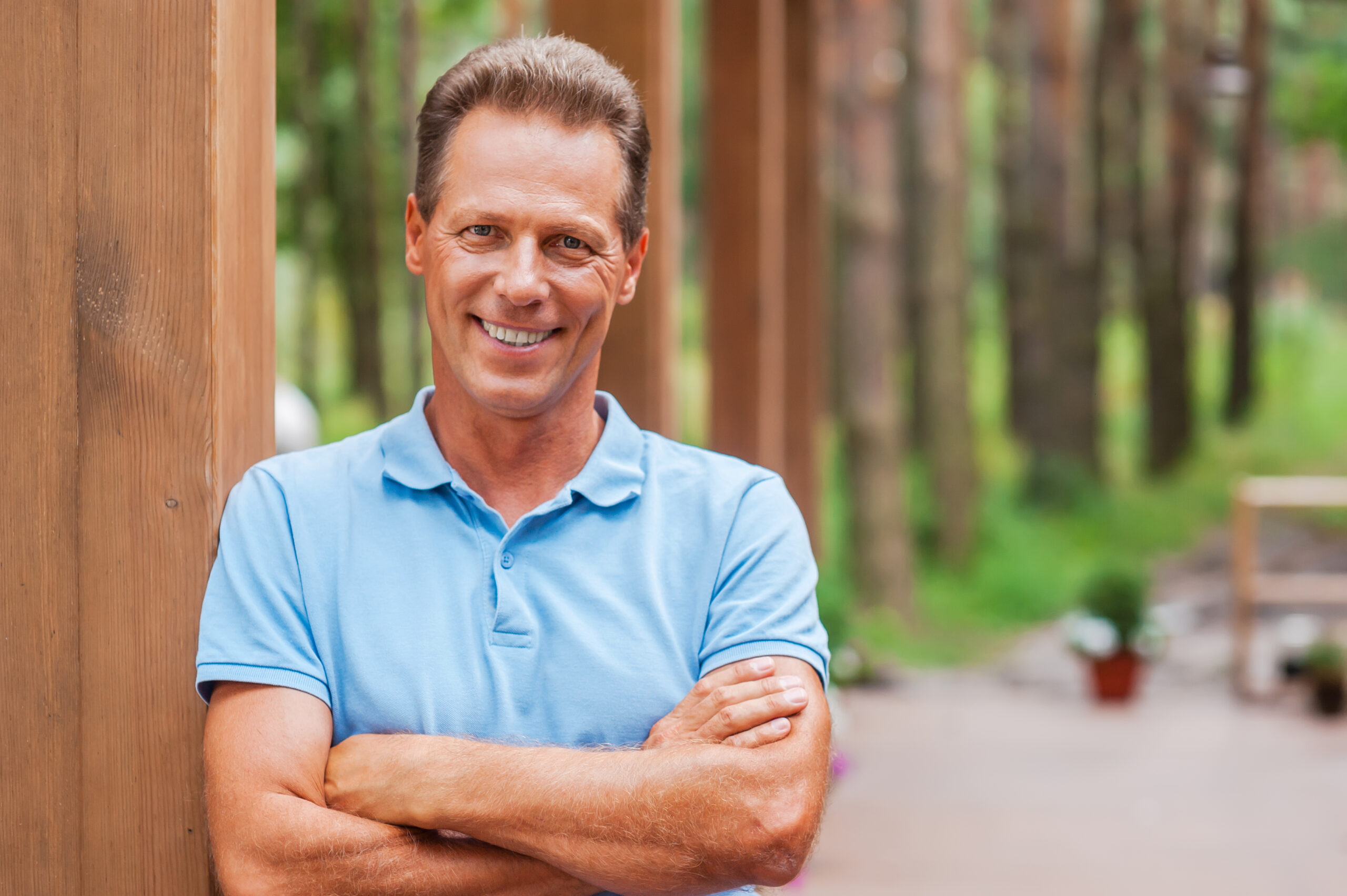 man folding arms standing by a tree