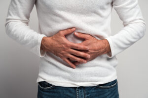 Close up view of the man holding hands on stomach feeling acute pain, suffering indigestion and nausea, duodenal ulcer. Indoor studio shot isolated on white background