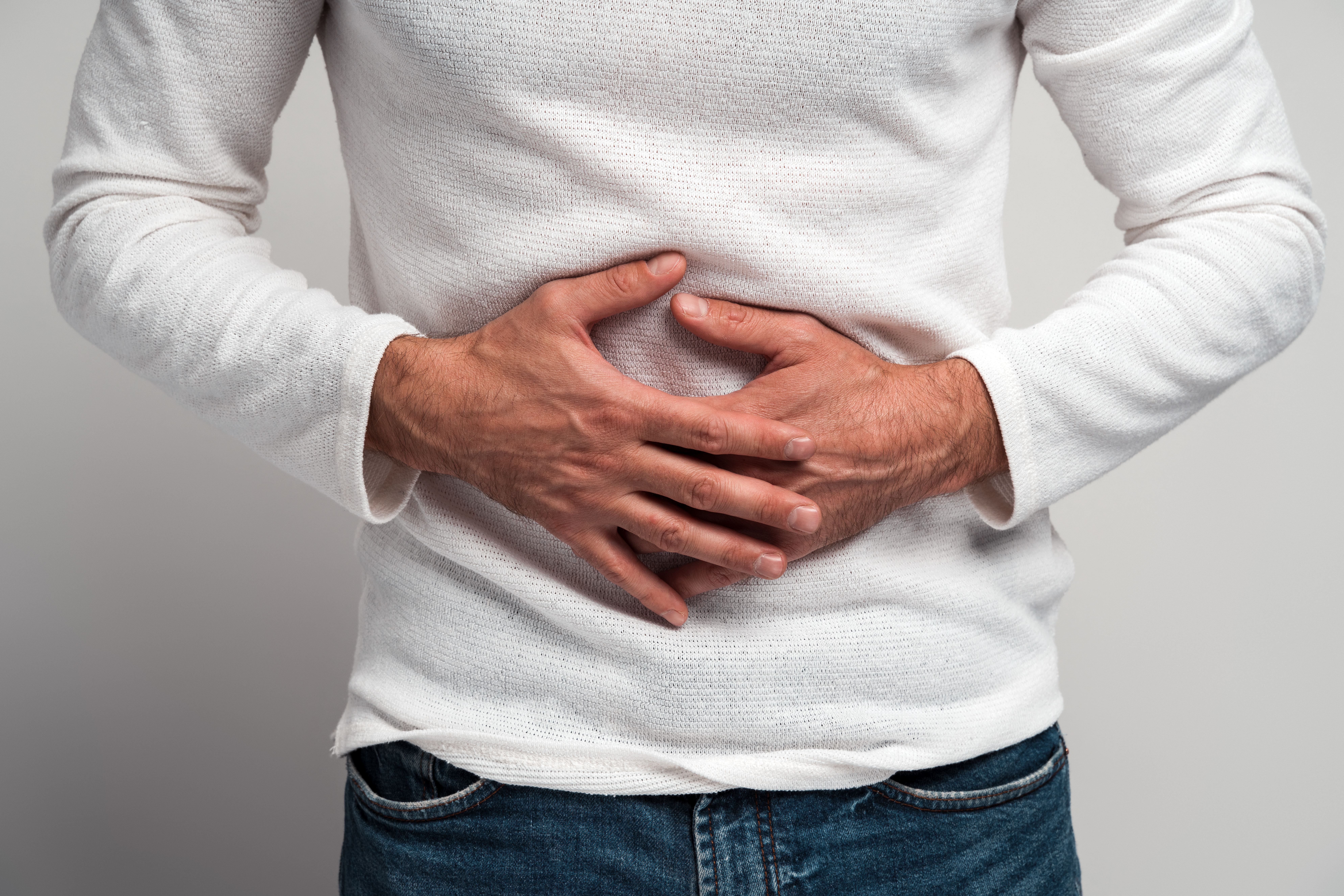 Close up view of the man holding hands on stomach feeling acute pain, suffering indigestion and nausea, duodenal ulcer. Indoor studio shot isolated on white background