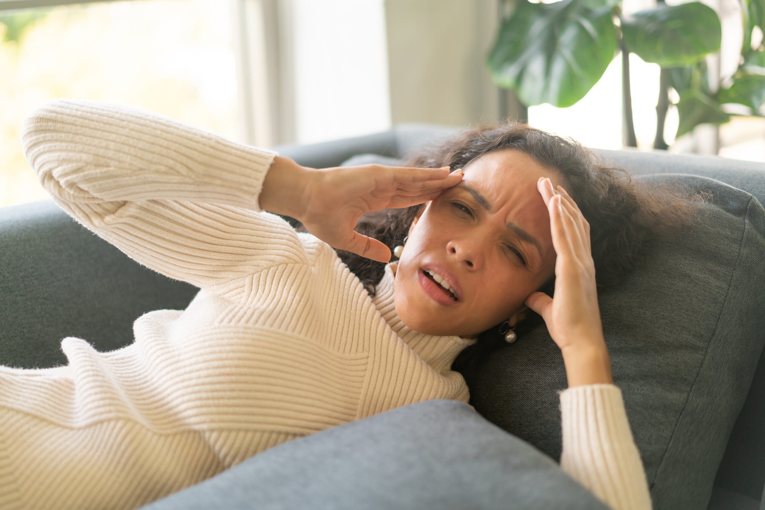 woman lying down on sofa with headache feeling